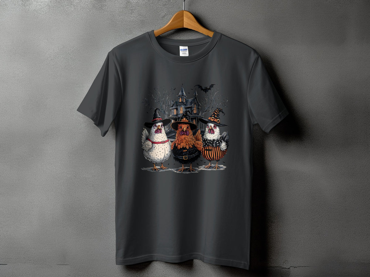 Three chickens in witch hats stand before a haunted house on a t-shirt.