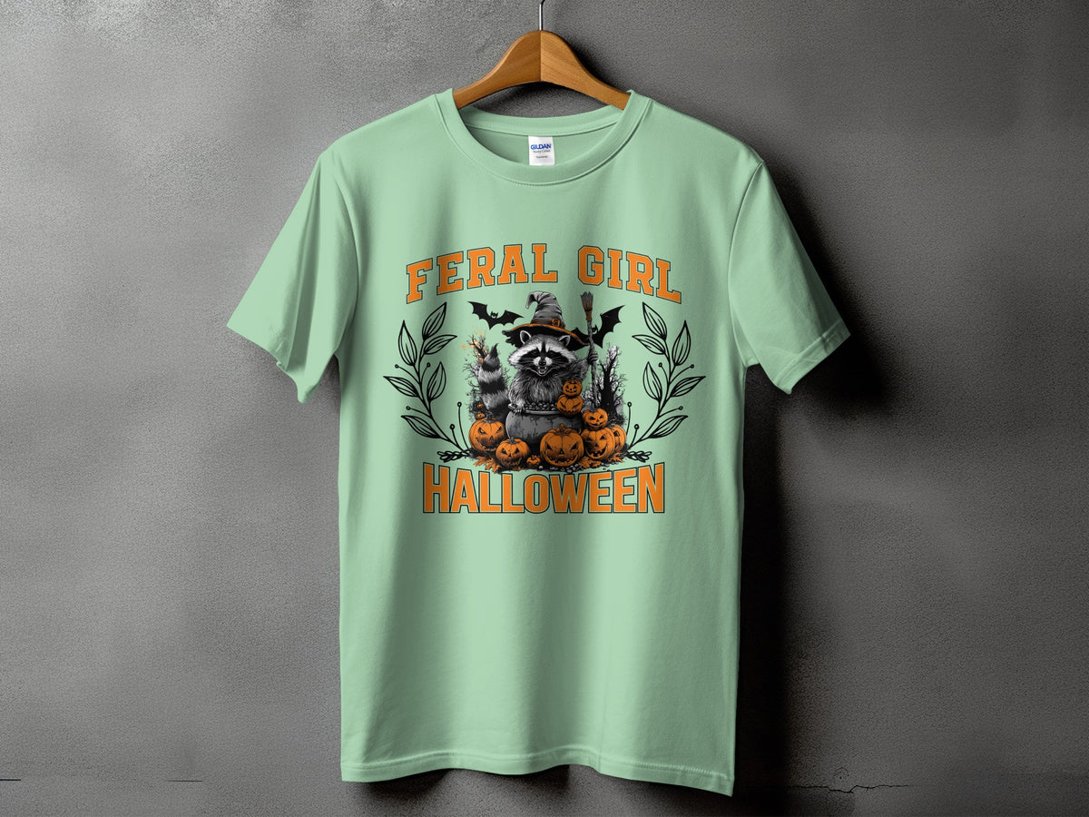 "Feral Girl Halloween" graphic with raccoon, pumpkins, bats, and witch's hat on a mint t-shirt.