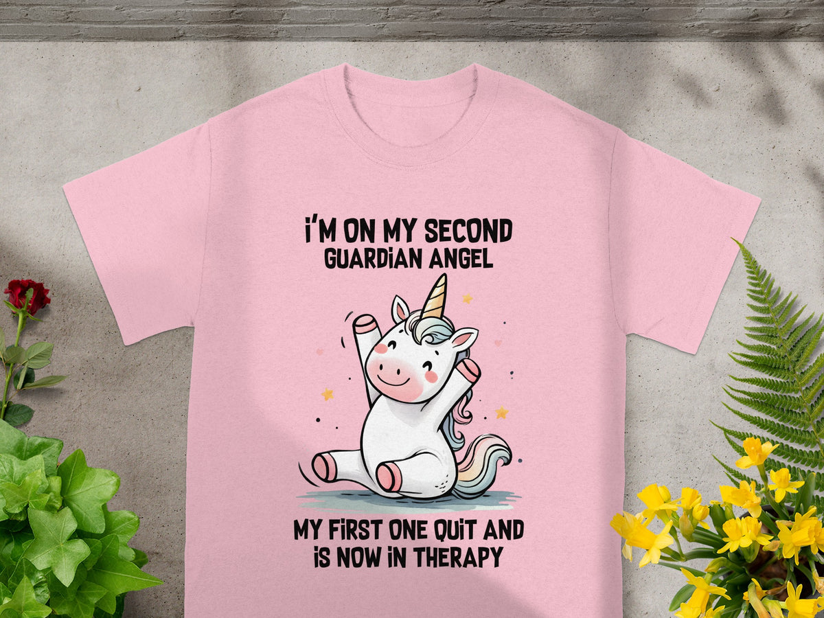 Pink t-shirt with unicorn graphic and text: "I'M ON MY SECOND GUARDIAN ANGEL MY FIRST ONE QUIT AND IS NOW IN THERAPY".