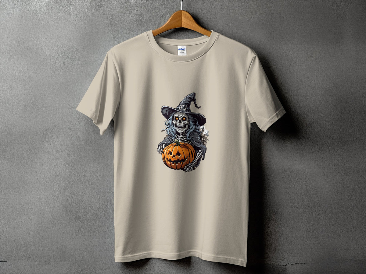 Skeleton in witch hat holding a carved pumpkin on a tan t-shirt.
