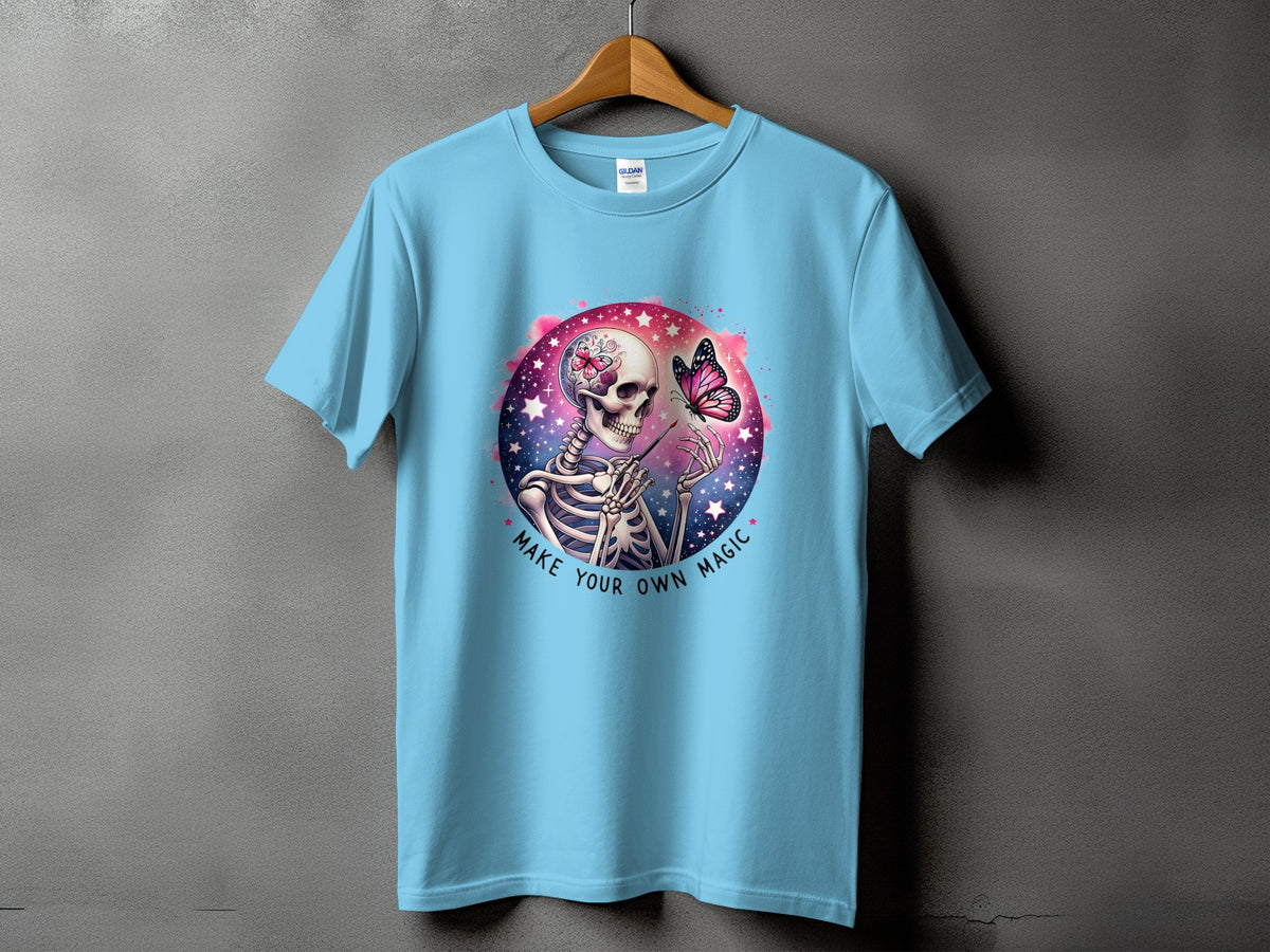 Light blue t-shirt with a skeleton, butterfly, and text "MAKE YOUR OWN MAGIC" graphic.