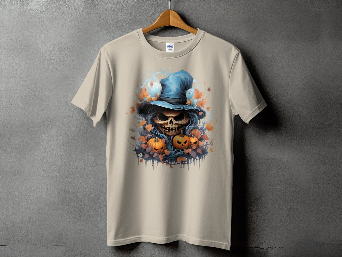 Skull in witch hat with pumpkins and fall leaves graphic on a tan t-shirt.